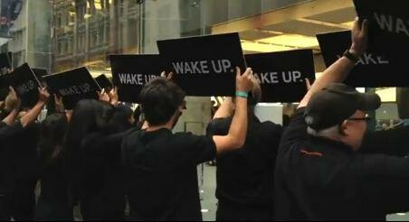 Schwarz gekleidete Menschen halten vor dem Apple-Store schwarze Schilder hoch, auf denen schlicht "Wake up" steht. (Bild: Screenshot YouTube/Blunty3000) Schwarz gekleidete Menschen halten vor dem Apple-Store schwarze Schilder hoch, auf denen schlicht "Wake up" steht. (Bild: Screenshot YouTube/Blunty3000)
