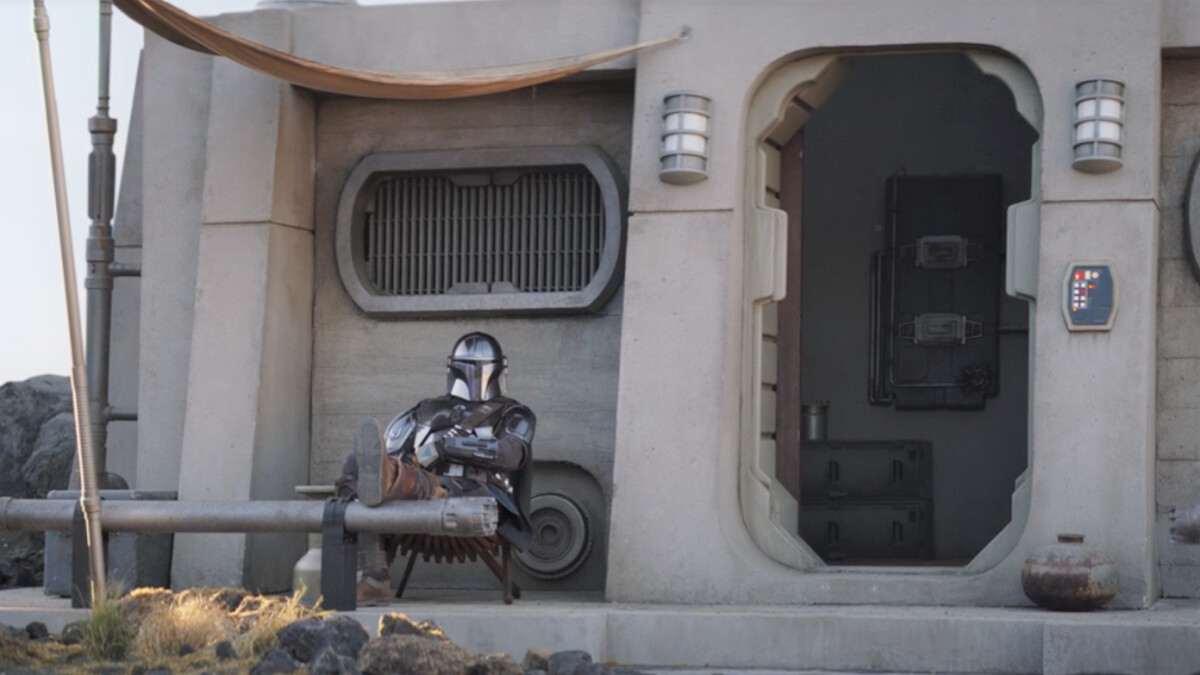 The Mandalorian: Western hero Din Djarin (Pedro Pascal) sits on his porch and looks at his child, Grogu.